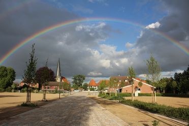 Ein weitläufiger Stadtplatz in Rehburg unter einem eindrucksvollen Regenbogen, mit Kirche und Häusern.