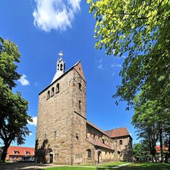 Stiftskirche Wunstorf, romanischer Baustil, charakteristischer Turm aus Sandstein, umgeben von Bäumen.