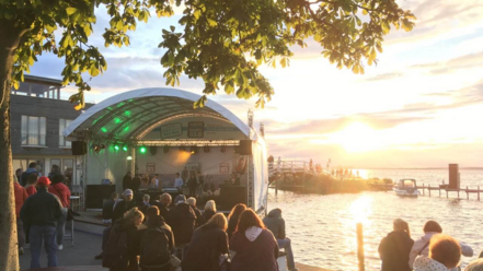 Menschen genießen einen Sommerabend auf der Seebühne am Steinhuder Meer bei Sonnenuntergang.